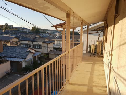 A long, covered outdoor walkway with a metal railing overlooks a dense residential neighborhood of houses in Japan.