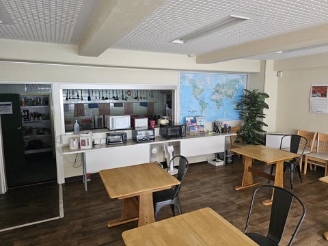A communal dining room with wooden tables, black chairs, and a counter with microwaves below a large world map on the wall.