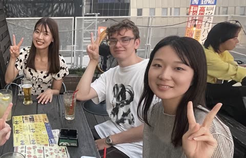 Three people sit at a table on an outdoor patio making peace signs for the camera.