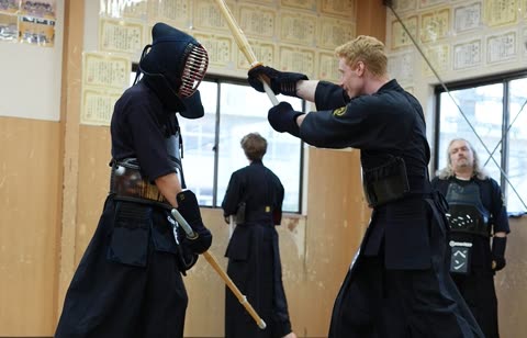 Two people in Kendo armor face each other with bamboo swords as one prepares to strike inside a dojo.