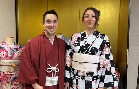 A man in a red kimono and a woman in a black-and-white patterned kimono stand together in front of a gold screen.