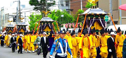 People in yellow and black carry ornate portable shrines down a city street.