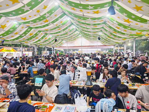 Many people eating and drinking under a striped tent.