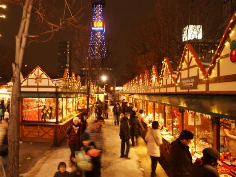 People shopping at night market with illuminated stalls and tower.