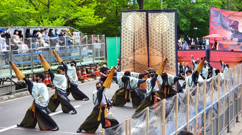 Performers in patterned robes manipulate large parasols during an outdoor performance.