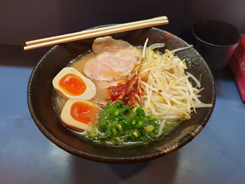 Bowl of ramen with sliced pork, soft boiled eggs, bean sprouts, and green onions.