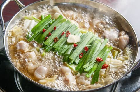Motsunabe bubbling in a pot, garnished with scallions and chili.
