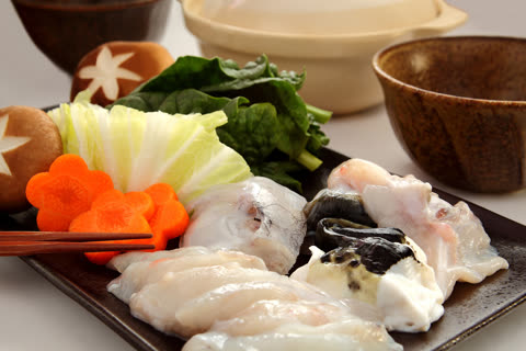 Raw pieces of fish, star-cut mushrooms, and flower-shaped carrots are arranged on a dark plate with fresh greens.