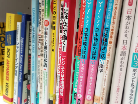 A row of colorful book spines with Japanese and English text are arranged vertically on a shelf.