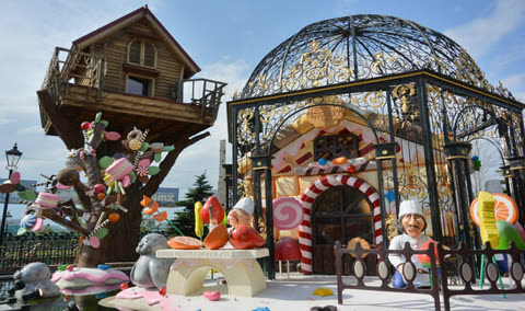 Candy-themed park structures with figures of chefs near a candy house and tree.