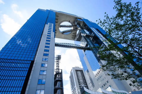 A low-angle view of two glass skyscrapers connected by a circular observation deck and walkways under a blue sky.