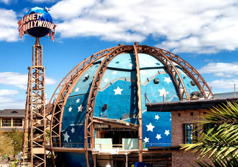 The Planet Hollywood building, a blue dome with white stars, sits under construction outdoors on a partly cloudy day.