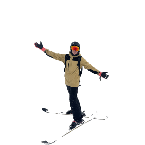 A skier in a helmet and goggles smiles with arms outstretched while standing on skis in a white, snowy setting.