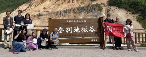 A group of people poses for a photo by a large wooden park sign, with a rocky, tree-lined valley in the background.
