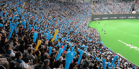 Large crowd in stadium seats holding up blue balloons.
