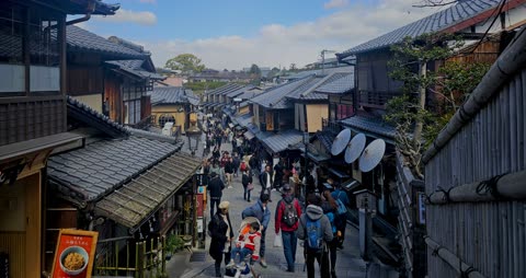 People walking down a narrow, sloped street lined with traditional Japanese buildings.