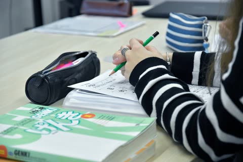 Person's hands writing with a green pencil on a paper at a desk.