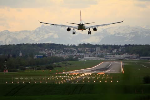 Airplane descending toward airport runway with mountains in background.