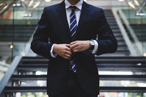 Man adjusts suit jacket near staircase.