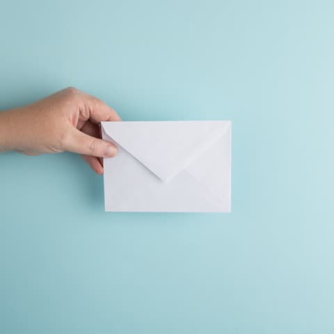 Hand holding white envelope against light-blue background.