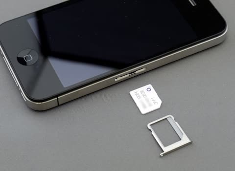 Black smartphone and SIM card on gray surface.