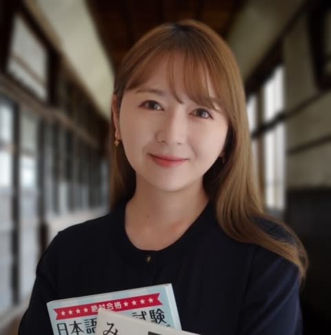 A woman with light-brown hair holds a book with Japanese text on the cover while standing in a hallway.