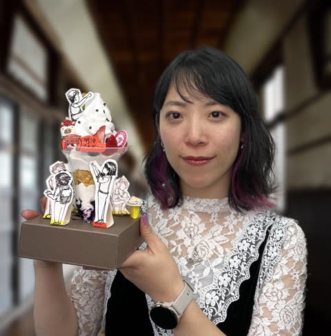 A woman with dark, purple-tipped hair holds a dessert parfait decorated with small paper cutouts in a blurred indoor hallway.