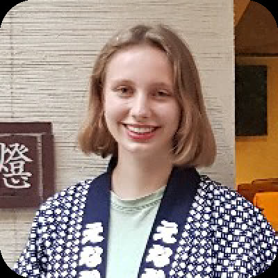 A woman with shoulder-length blonde hair smiles while wearing a patterned blue and white Japanese jacket indoors.